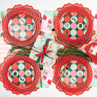 Overhead grid view of four red and green plaid holiday plates layered neatly over red die-cut scalloped paper chargers.