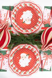 Overhead grid view of four vintage Santa plates layered over red plaid paper chargers with honeycomb ornaments in the center.