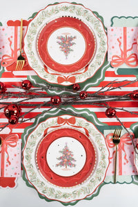 Symmetrical flat lay of four vintage Christmas tree place settings arranged on a striped table runner with red ornaments.