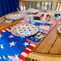 Fourth of July table runner with stars and stripes design, styled with matching plates, napkins, and wooden cutlery.