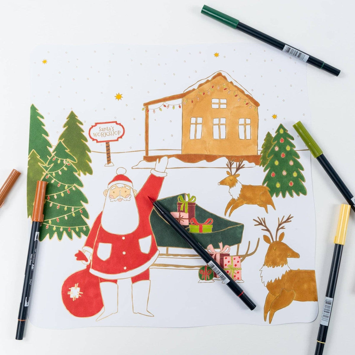 Overhead view of a fully colored Christmas paper placemat surrounded by scattered dual-tip markers.
