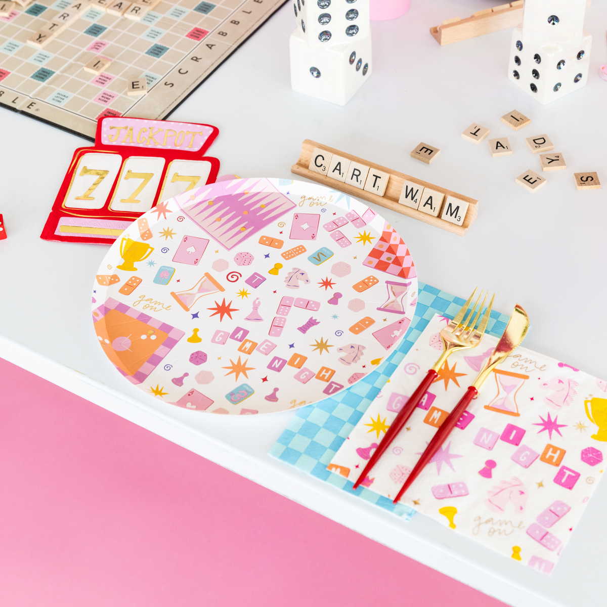 Game night round paper dinner plate on a blue checkered napkin styled with a Scrabble board, white dice decor, jackpot slot machine shaped plate, gold cutlery, and game night cocktail napkins