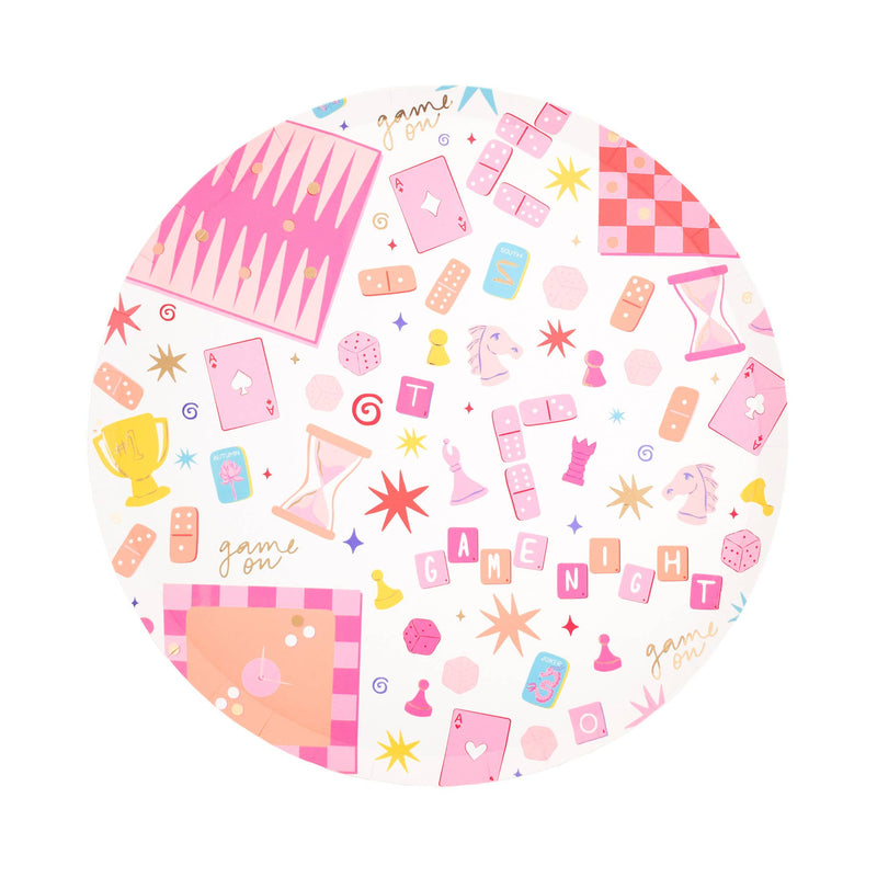 Single game night round paper dinner plate on white background showing pink all-over print of cards, dice, dominoes, chess pieces, backgammon, hourglass, trophy, and "GAME NIGHT" tile lettering