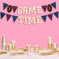 Gold foil game time banner hanging above football-themed party table with gold cups and plates