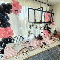 A styled Pink and black Halloween party tablescape in a room with black and pink balloon garlands, ghost decorations, a pink-and-white striped table runner, plates, and napkins.
