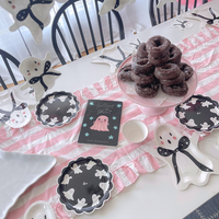 Pink Halloween tabletop display including black scalloped plates with white ghost illustrations, a pink and white striped runner, ghost-shaped napkins, and a book.