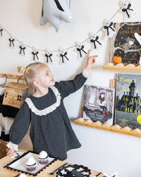 Child in a polka dot dress pointing at Halloween-themed ghost banner along with other Halloween decorations in the room. 