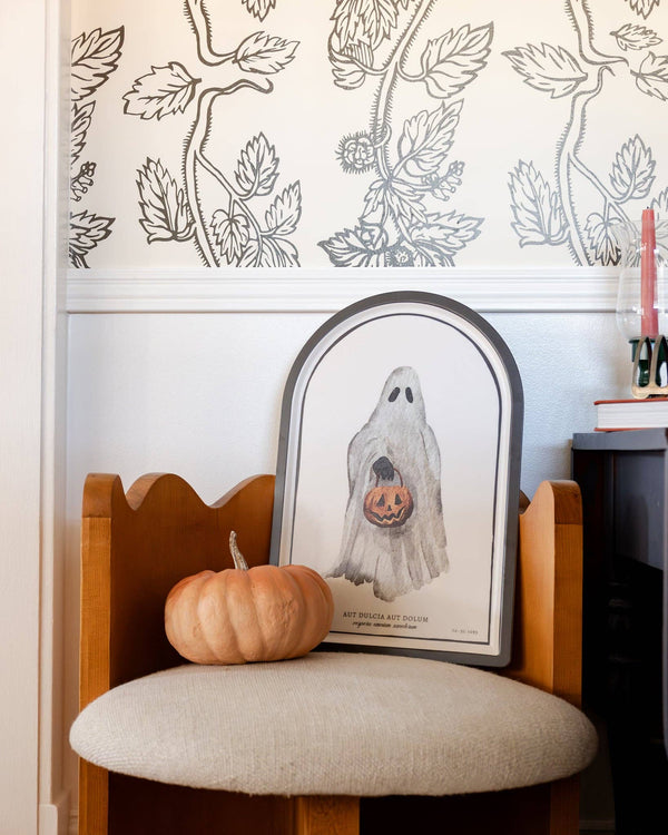 Ghost bamboo tray leaning on a wood chair as wall art beside a small orange pumpkin