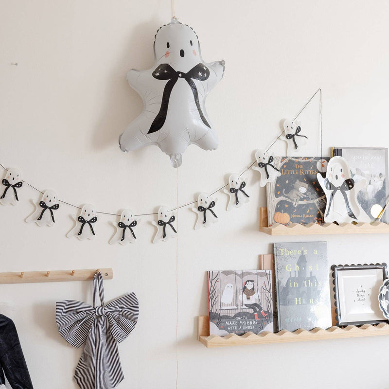 Grey ghost mylar balloon with a black star bow hanging on a wall above a ghost garland and a set kids party table