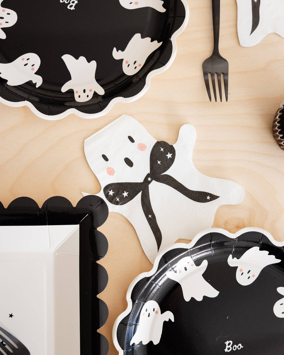 A piece of ghost-shaped Halloween cocktail napkins styled on a cocktail table beside other ghost related Halloween decorations.