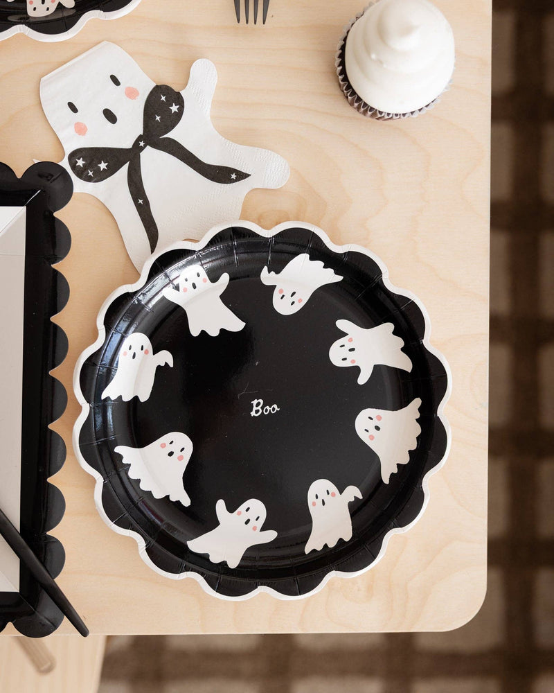 Scalloped ghost paper plate styled with cupcakes on a black and white themed Halloween table.
