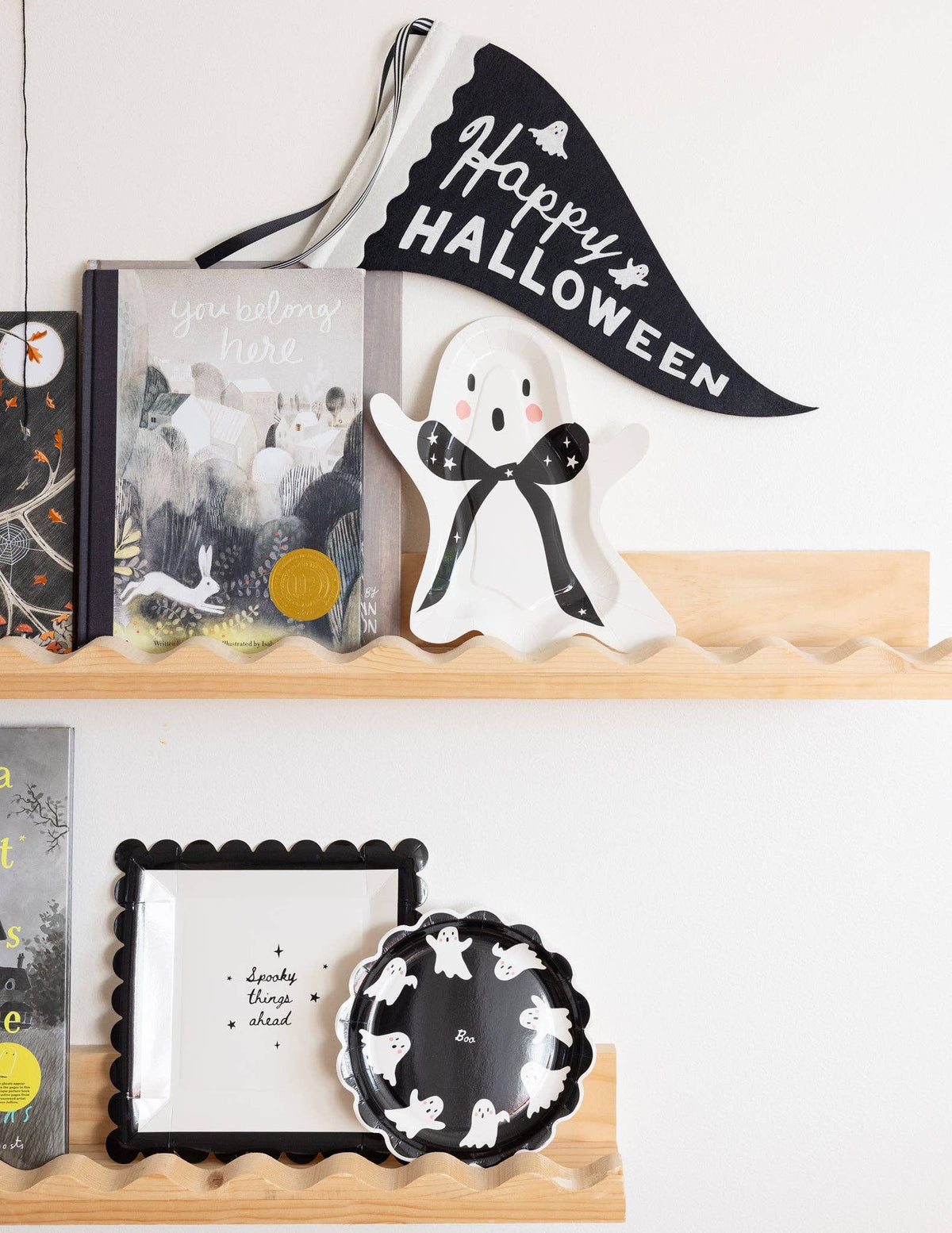 Decorative Halloween shelf featuring the ghost paper plate with other halloween figurine, books, and banner on a white wall.