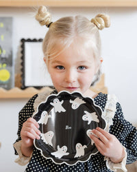 Child holding a black plate with ghost decorations in a room setting.