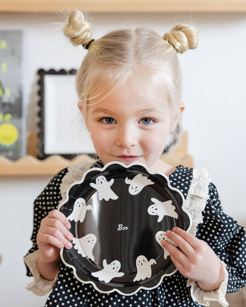 Child holding a black plate with ghost decorations in a room setting.