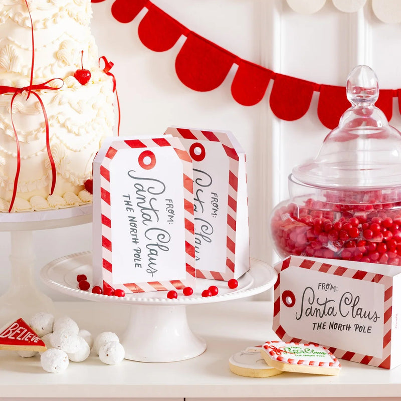 Detail scene with “Believe” pennant and tag Christmas treat boxes bags beside cake and candy jars