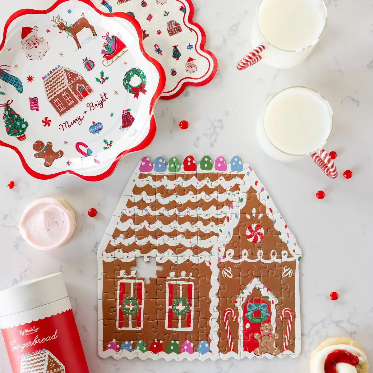 Gingerbread house jigsaw puzzle on a marble counter with milk and frosted cookies; Merry + Bright plates shown separately, not included