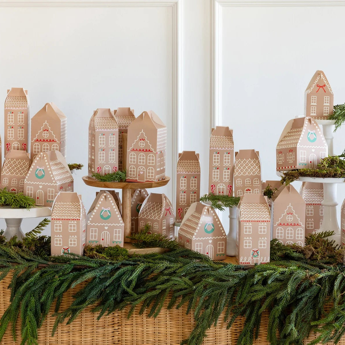 Large display of the 25 gingerbread house treat boxes arranged as a village, set on a table with evergreen garland.
