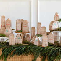 Large display of the 25 gingerbread house treat boxes arranged as a village, set on a table with evergreen garland.