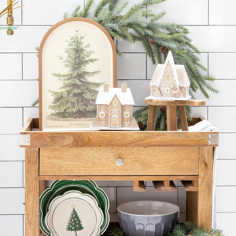 Christmas village display featuring the Gingerbread Chalet on a wooden cart next to other gingerbread house designs and holiday decor.