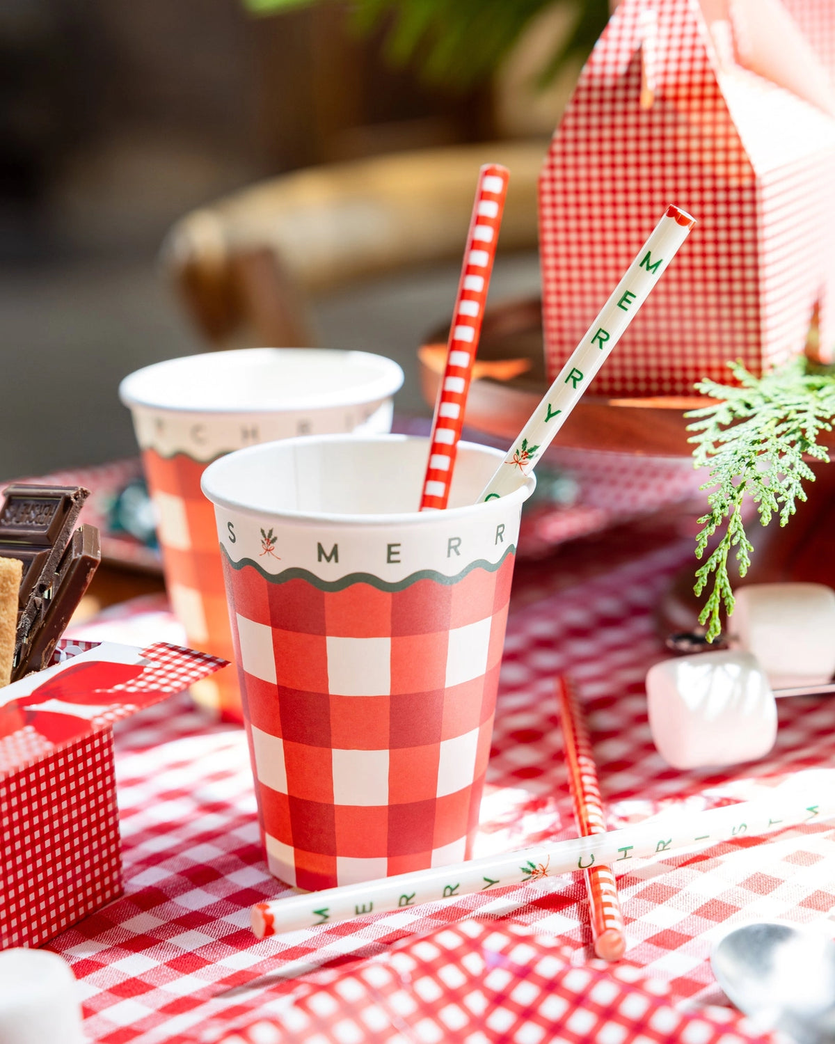 Gingham Christmas cups with red-striped paper straws on a rustic table.