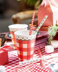 Gingham Christmas cups with red-striped paper straws on a rustic table.