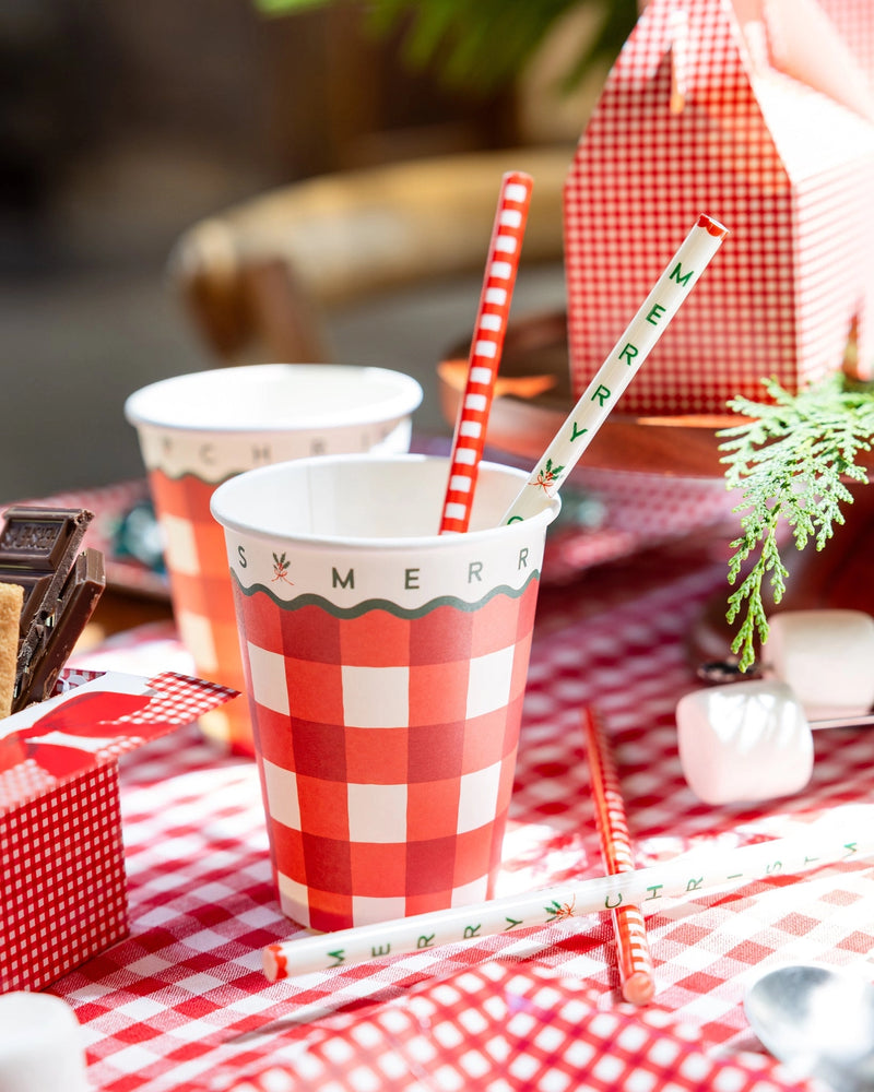 Gingham Christmas cups with red-striped paper straws on a rustic table.