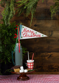 A gingham cup with a straw beside a thermos and a "Merry Christmas" pennant flag.