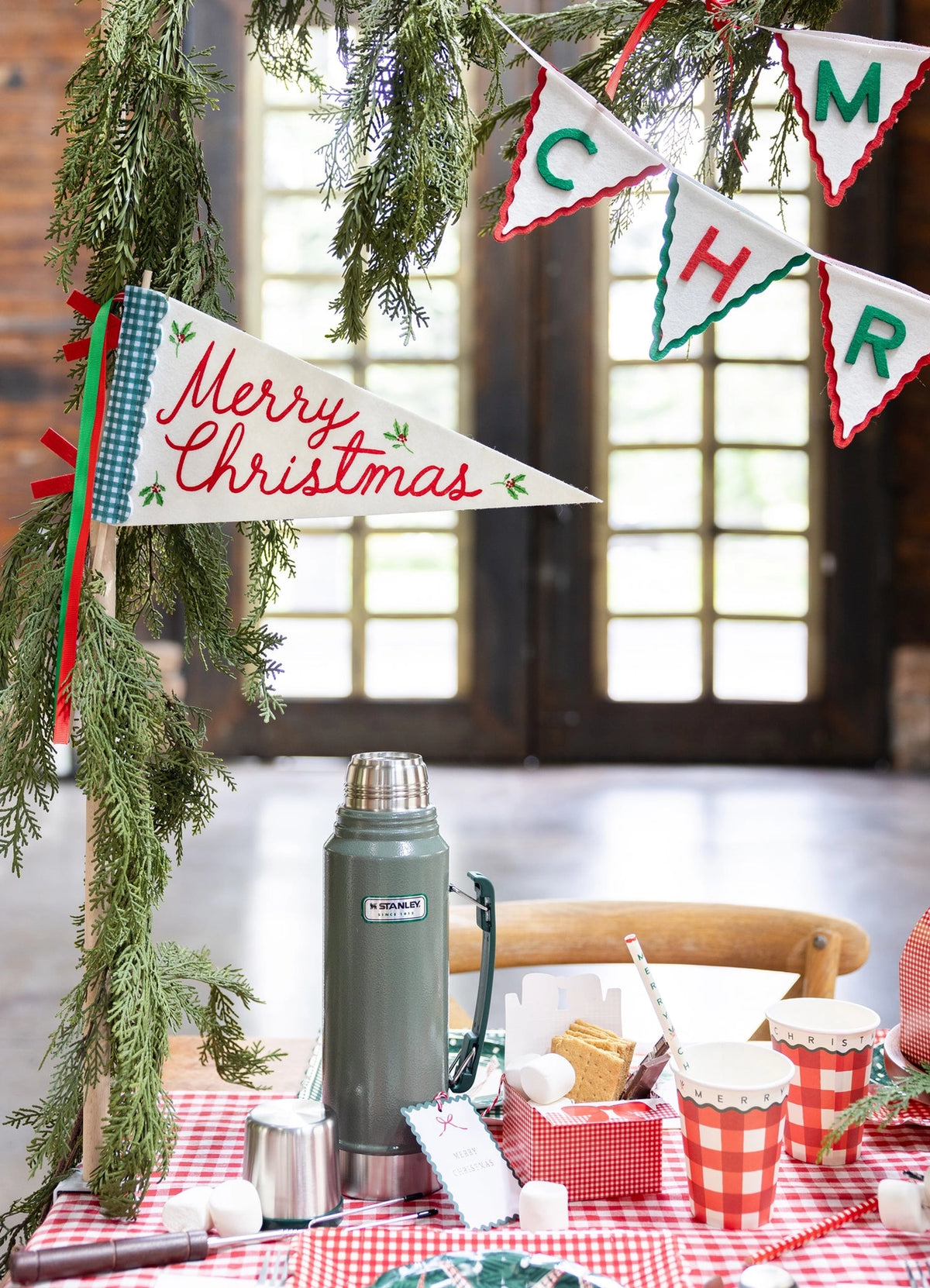 A holiday drink scene with a thermos, gingham cups, and a "Merry Christmas" pennant flag.