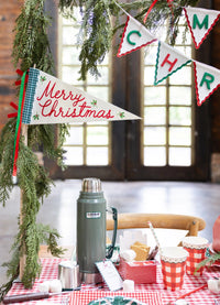 A holiday drink scene with a thermos, gingham cups, and a "Merry Christmas" pennant flag.