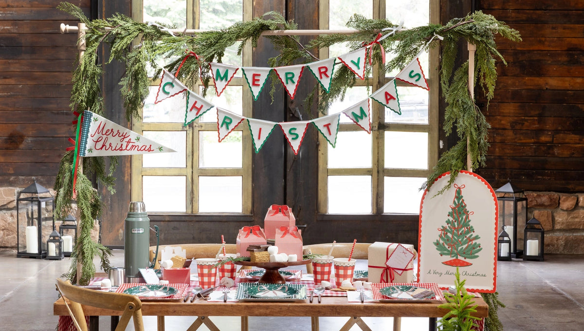 Rustic window room with a "Merry Christmas" felt banner, red gingham treat boxes on a cake stand, and a full plaid table.