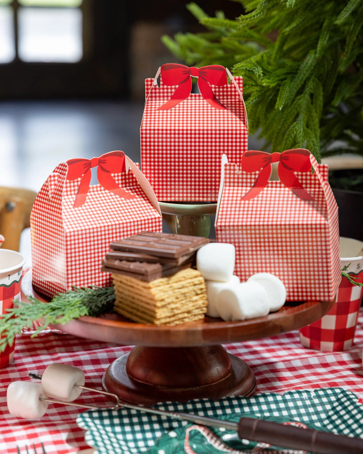 Red gingham treat boxes on a wood cake stand with s'mores and marshmallows.