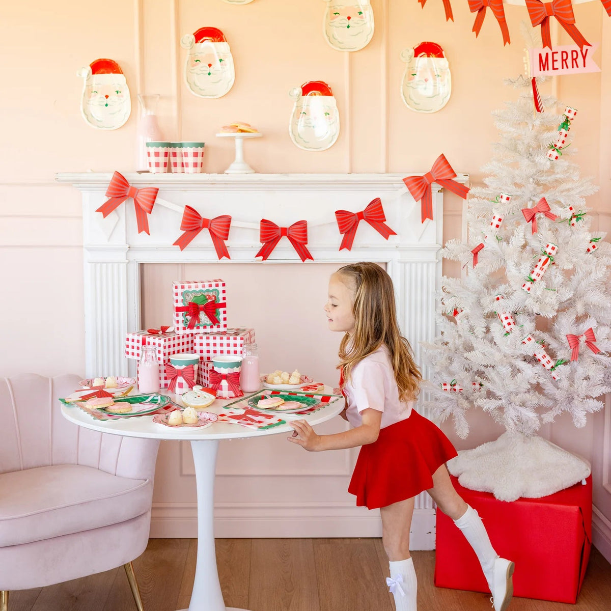 Child standing by a gingham-themed Christmas party table set with plates, treats, and packaged Christmas poppers and crackers as decorations.