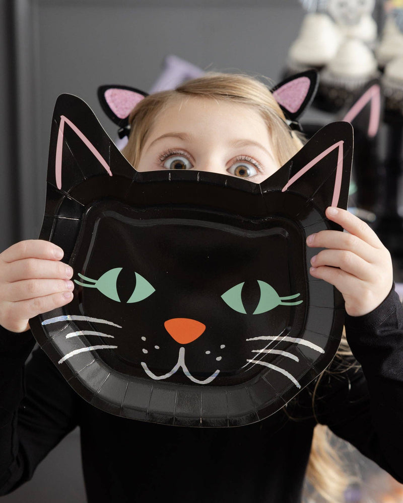 Young girl holding the cat face plate up to her face like a mask at a Halloween party, showing the 9" scale — playful, kid-friendly lifestyle shot.