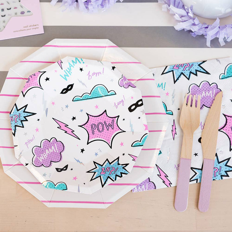 Flat lay of a superhero themed party table with comic book pop art plates, lightning bolt napkins, and purple wooden cutlery.