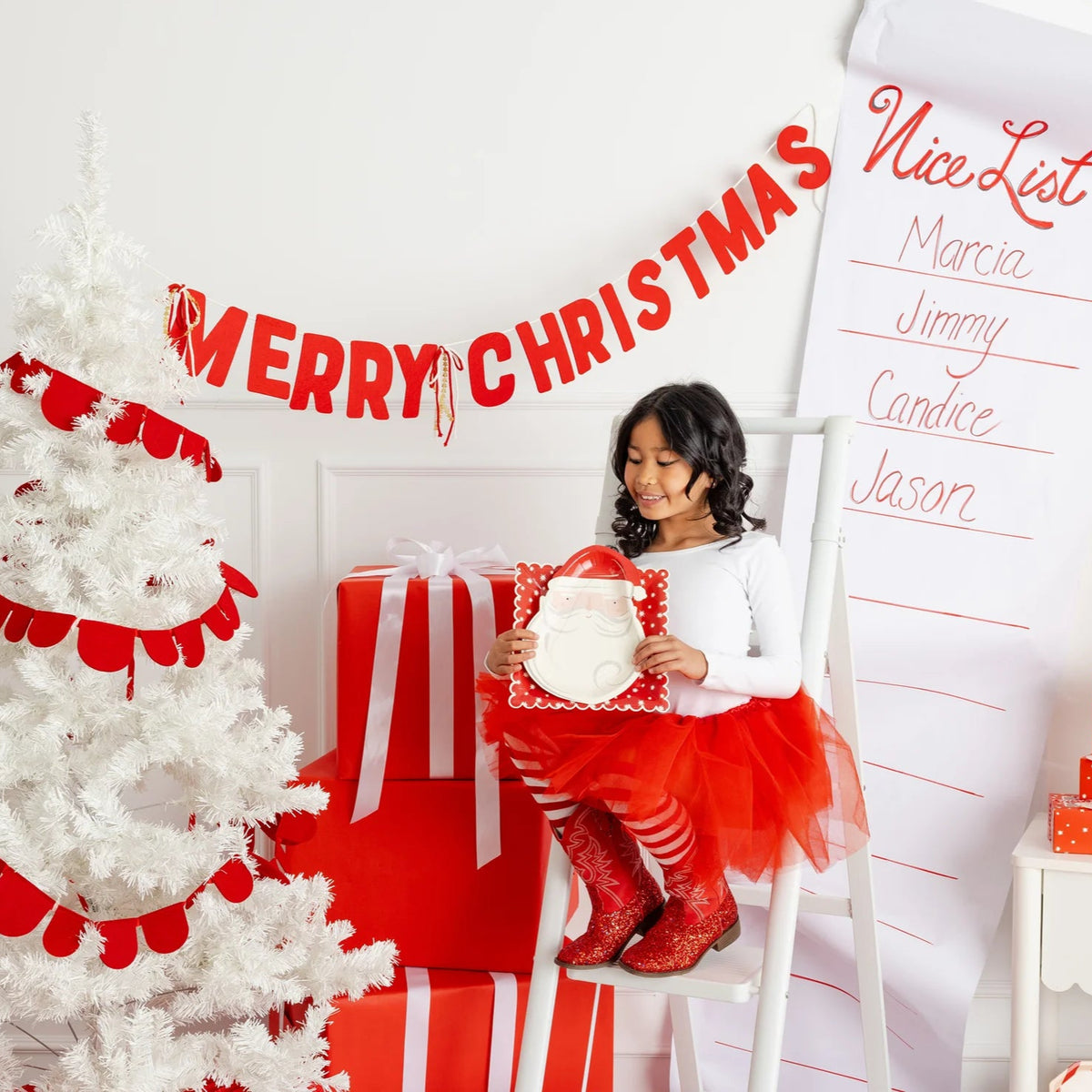 Young girl sitting next to a white tree and Nice List, holding a small plate which would layer on top of the large Christmas dinner plates.