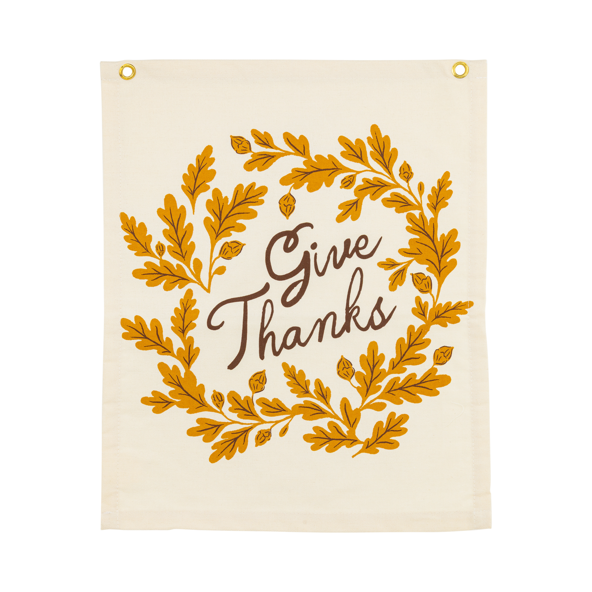 Overhead studio view of a rectangular off-white canvas banner featuring a mustard yellow oak leaf wreath and black Give Thanks text.