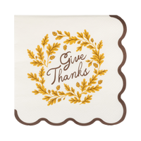 Cream cocktail napkin with "Give Thanks" text, brown and yellow accents, and a wavy brown edge, front view.