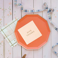 Peach “Give Thanks” cocktail napkin centered on an orange octagon plate with plaid ribbon and confetti.