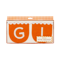 Close-up of the Give Thanks banner packaging in an orange gingham box, highlighting the scalloped orange felt and cream stitched letters.