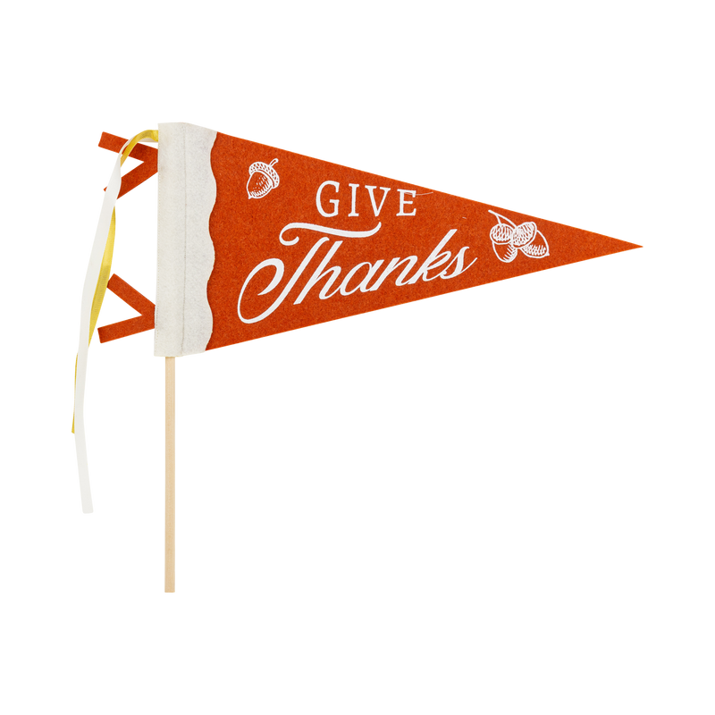 "GIVE THANKS" brown felt pennant with cream script and a small pumpkin accent on a wood dowel with striped ribbon, front view on white background.