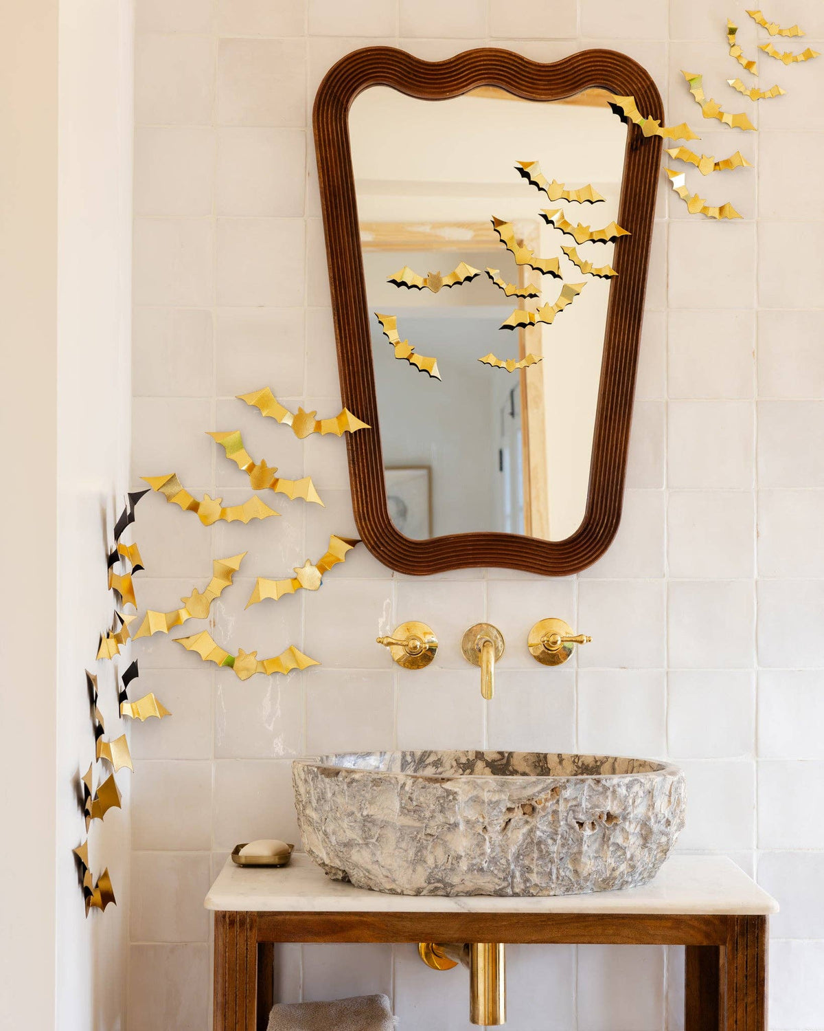 Bathroom vanity with decorative mirror, sink, and gold bats arranged in a flight-swarm pattern on a wall.