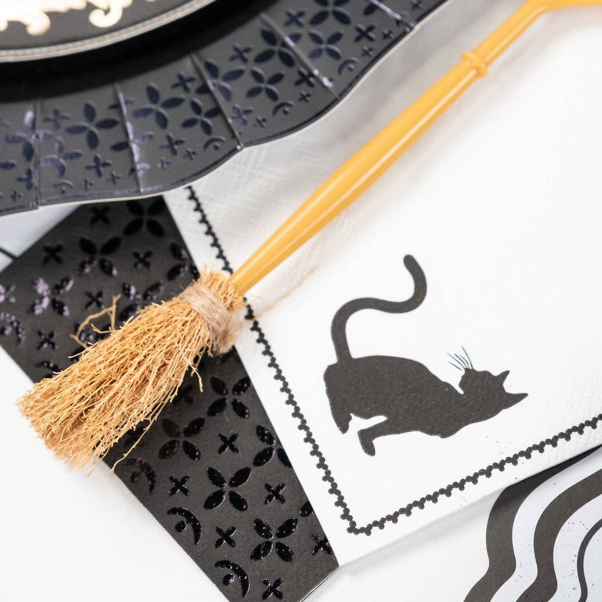 Close up of a gold decorative broomstick fork resting diagonally across a white and black cat silhouette paper cocktail napkin.