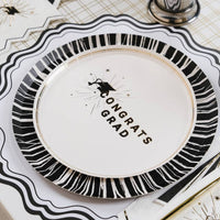 A close up of a Congrats Grad dessert plate with a gold foil striped rim for a Cap and Champagne celebration.
