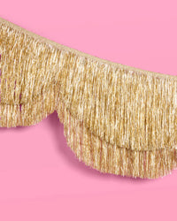 Single gold foil fringe banner curved on pink background showing full scalloped silhouette