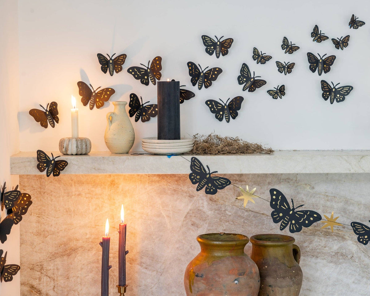 Close-up of gold foil moths on a marble shelf catching candlelight, showing the different sizes and gold detail against black paper.