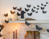 Close-up of gold foil moths on a marble shelf catching candlelight, showing the different sizes and gold detail against black paper.