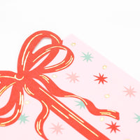 Extreme close-up of the top left corner of the pink paper napkin highlighting the die-cut red ribbon and shiny gold foil starbursts.