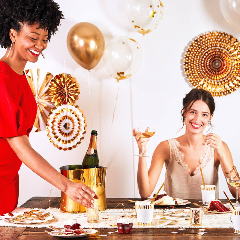 Two women celebrating at a dinner table decorated with metallic gold party fans, balloons, and a champagne bucket.