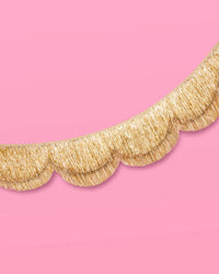 Close-up of gold foil scalloped fringe banner edge on pink background showing texture
