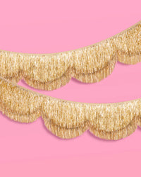 Two gold scalloped fringe banners layered on pink background, close-up detail shot